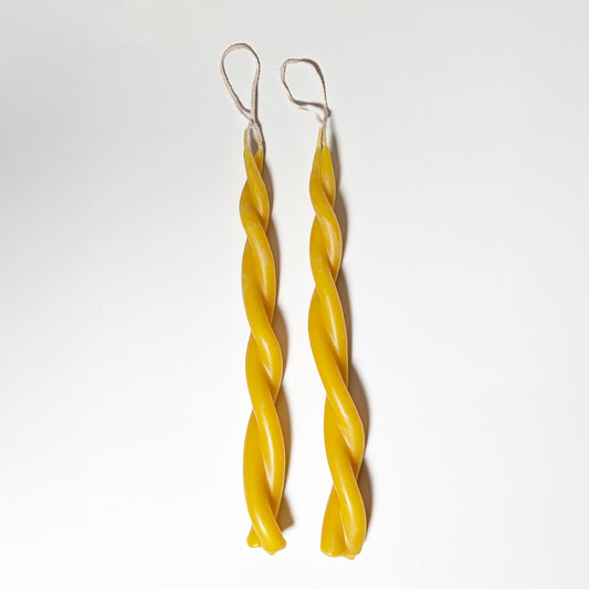 Two hand-dipped Twin Flame beeswax candles with twisted forms and cotton wicks, shown on a white background highlighting their natural golden hue and smooth finish.