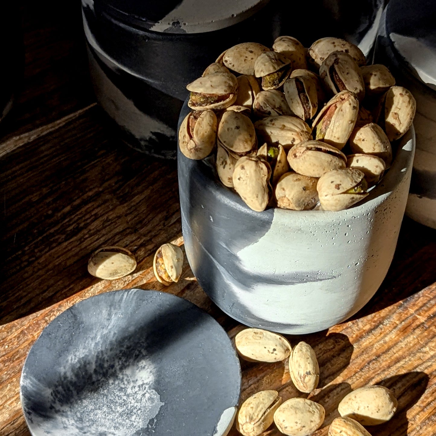 Marbled cement vessel from Nightcap Noir repurposed as a small dish filled with pistachios, illustrating reusable design.