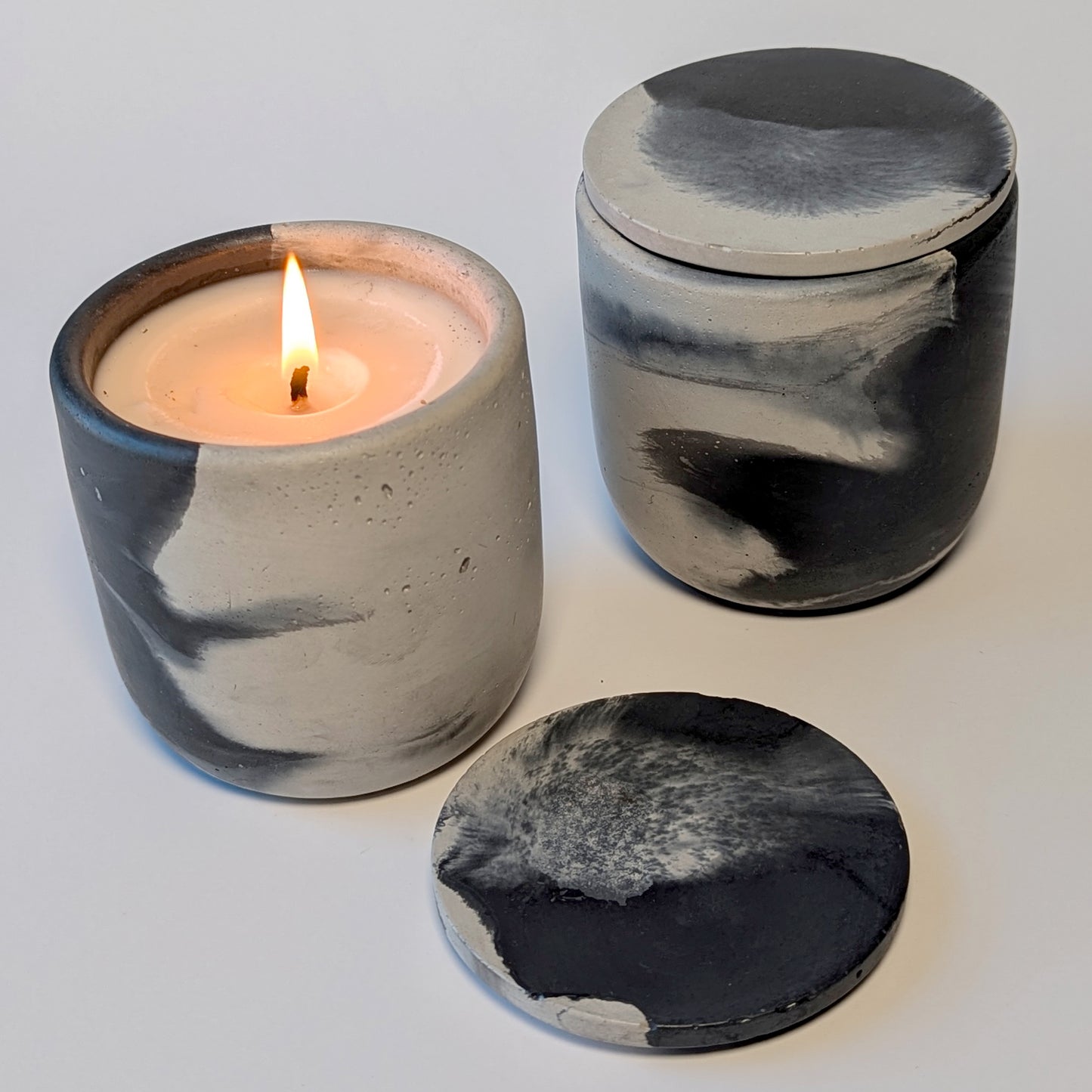 Nightcap Noir candle burning, flame glowing against the smoky cement vessel surface.