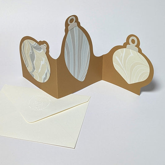 The Suminagashi trifold ornament notecard backside, standing open on a white background, highlighting three soft-toned marbled paper ornaments mounted on shimmering gold cardstock.