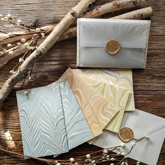 A collection of beautifully crafted notecards with hand-marbled patterns, displayed alongside matching envelopes and metallic gold wax seals.