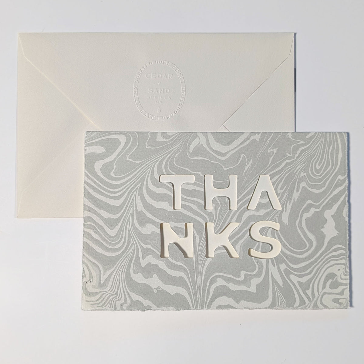 Handmade Suminagashi Thanks Notecard in Smoke with flowing gray and white marbling, cut-out THANKS lettering and matching envelope.