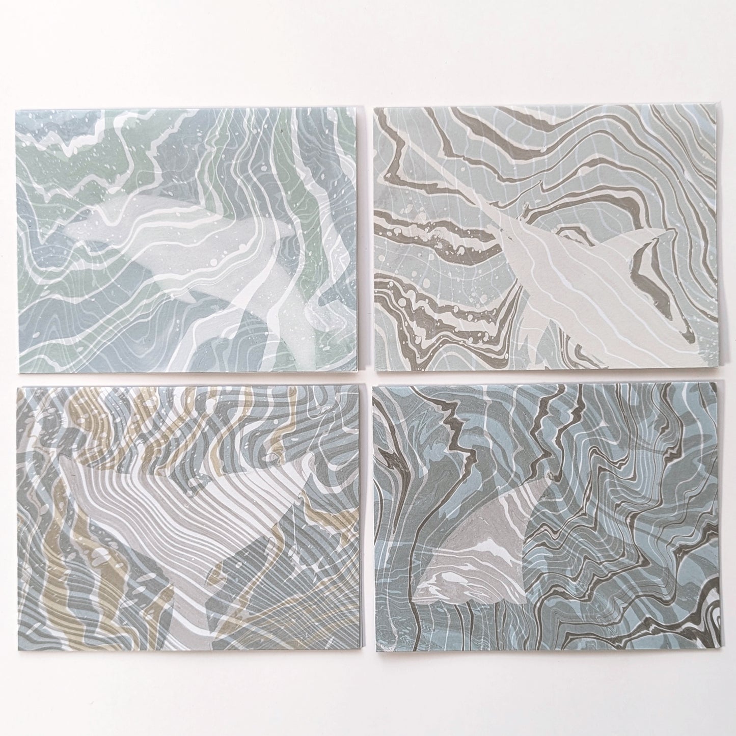 Set of four Marine Fauna Suminagashi notecards from the Fin Series, each featuring hand-marbled backgrounds with masked silhouettes of marine life: dolphin, swordfish, whale tail, and shark fin.