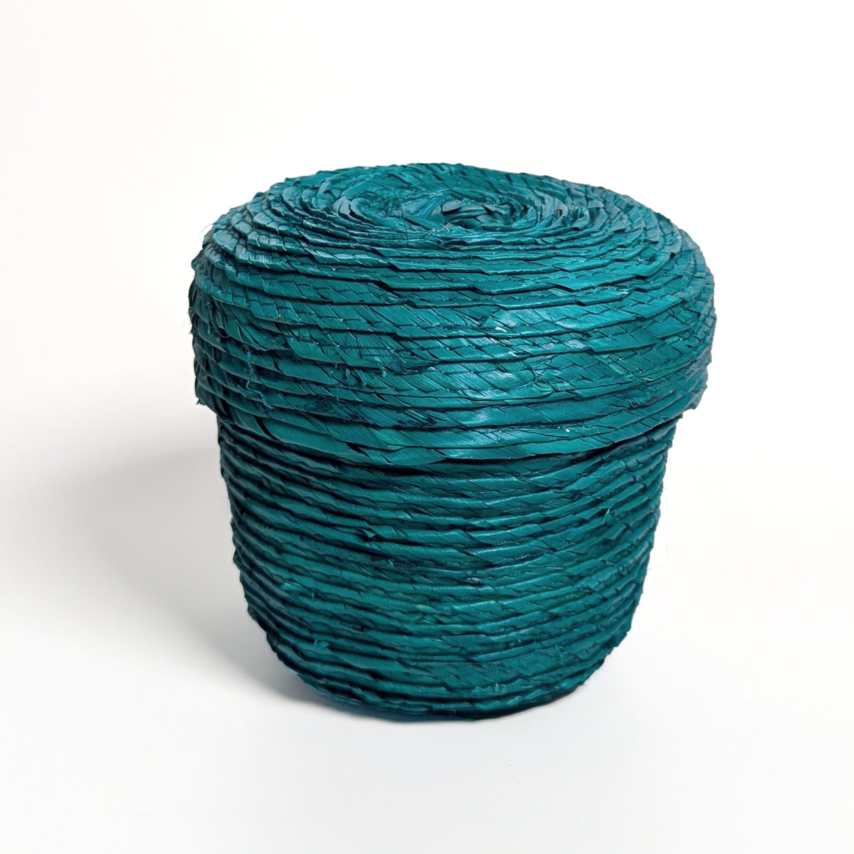 Lidded teal palm leaf woven basket, on a white surface.