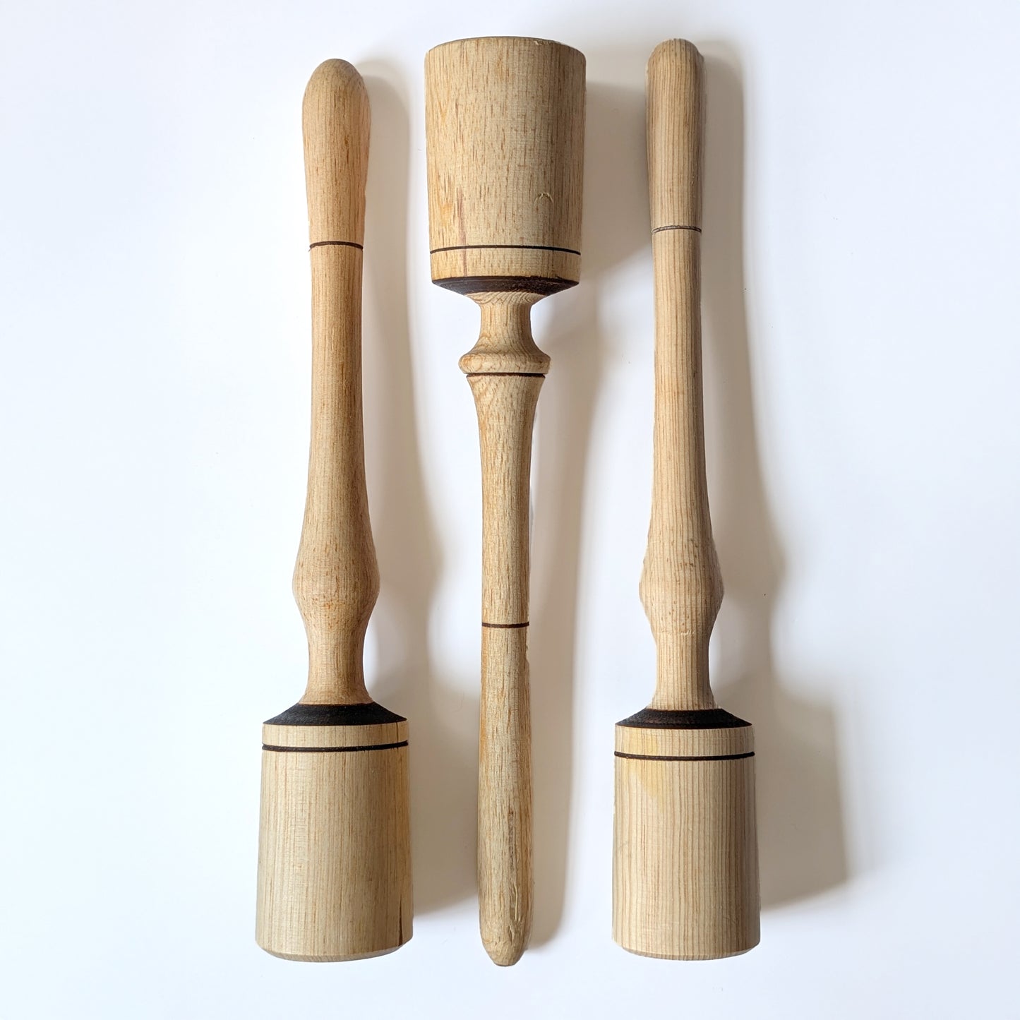 Three wooden narrow pestles tools with varied accents on a white background