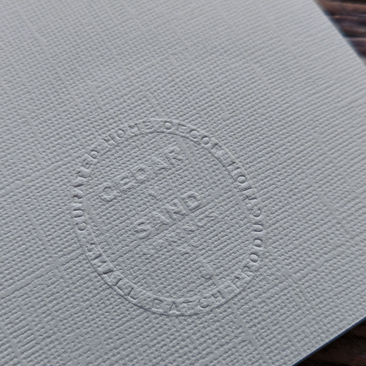 Textured warm gray Wheat Suminagashi notecard showing the embossed CEDAR Y SAND studio insignia on the reverse.