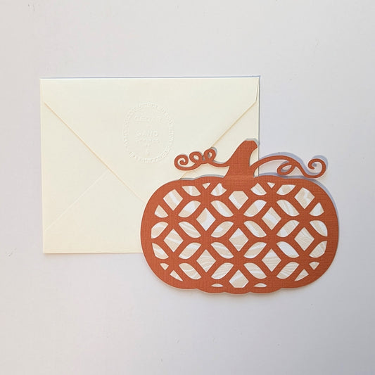 Hand-cut pumpkin lattice notecard with marbled paper backing beside embossed envelope on neutral background.