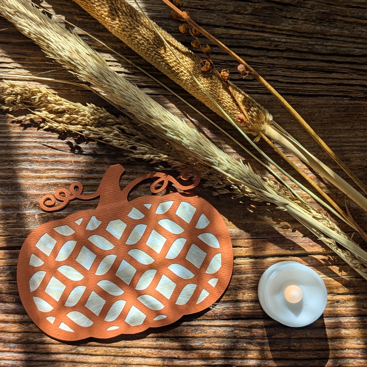 Pumpkin Lattice Notecard with Autumn Glow Tealight and dried stems under warm sunlight on rustic wood.