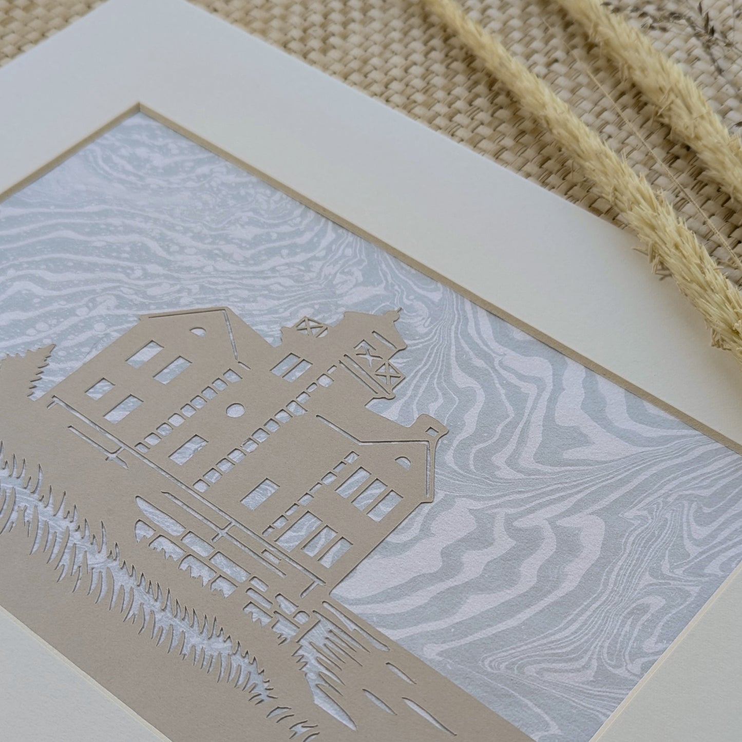 Detail view of Cedar Point Lighthouse cut-paper silhouette on foggy blue marbled suminagashi paper, showing swirling tide-like ink lines.