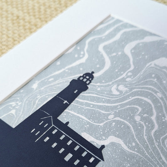Detail view of Montauk Lighthouse cut-out layered over pale blue suminagashi paper showing marbled ink swirls and silhouette precision.”