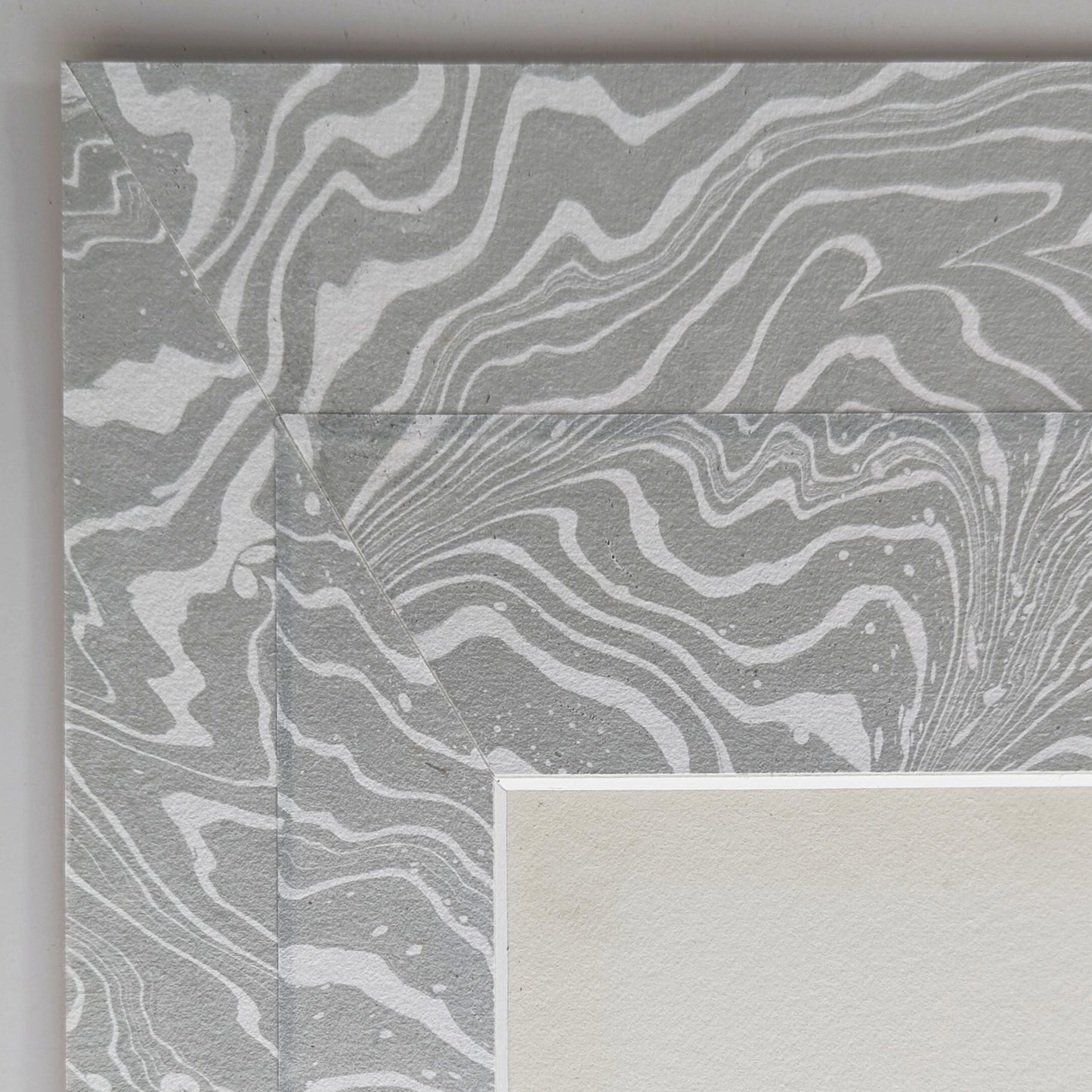 Close view of cool gray and off white suminagashi Hosho paper collaged mat surrounding painting.