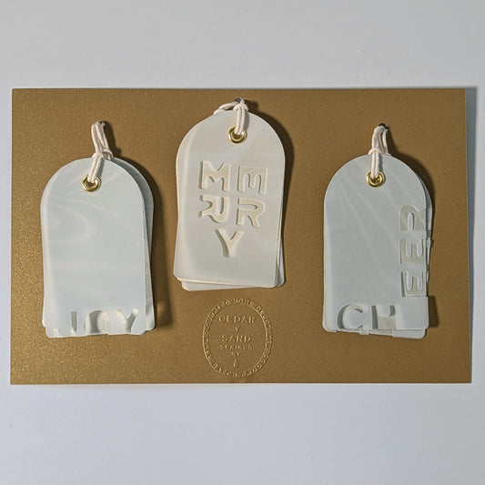Set of six Suminagashi gift tags—JOY, MERRY, CHEER—mounted on a gold backing card with the CEDAR Y SAND embossed seal.