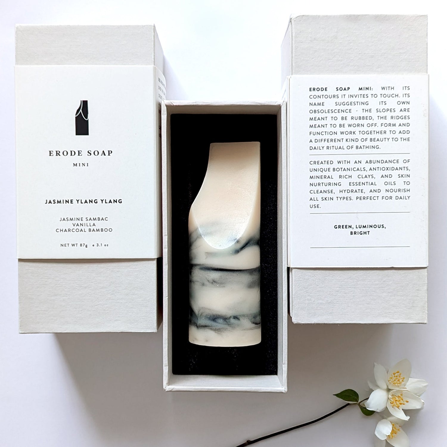 A sculptural erode soap mini in jasmine ylang ylang rests in its open white box with printed packaging, styled as a minimalist everyday bathing object.