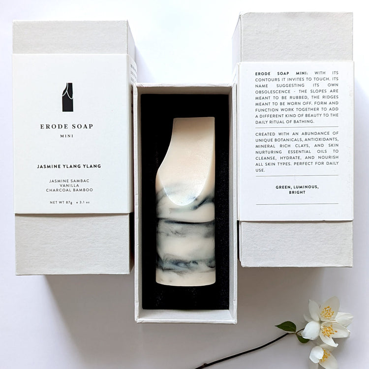 A sculptural erode soap mini in jasmine ylang ylang rests in its open white box with printed packaging, styled as a minimalist everyday bathing object.