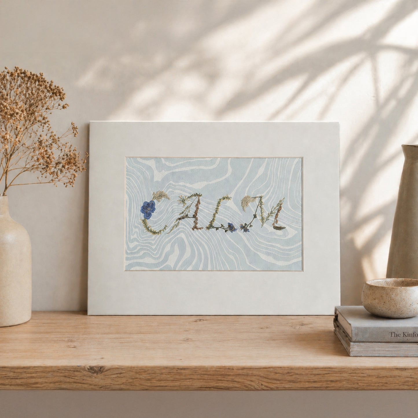 Pressed floral word “CALM” on blue Suminagashi marbled paper, matted botanical artwork styled in a neutral interior setting