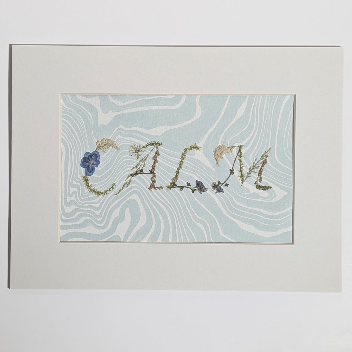 Pressed floral word “CALM” formed with real botanicals on hand-marbled Suminagashi paper, matted artwork by CEDAR Y SAND