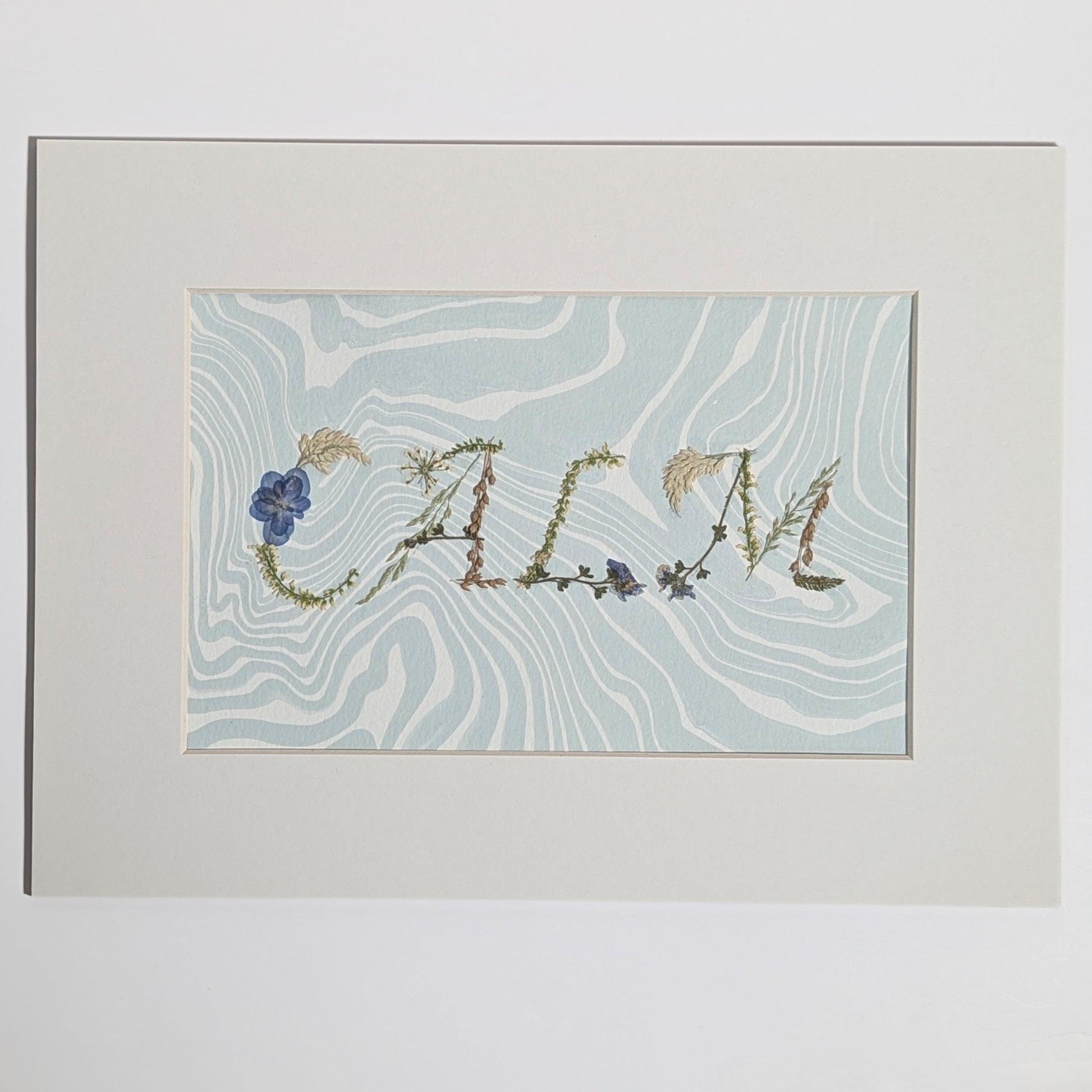 Pressed floral word “CALM” formed with real botanicals on hand-marbled Suminagashi paper, matted artwork by CEDAR Y SAND