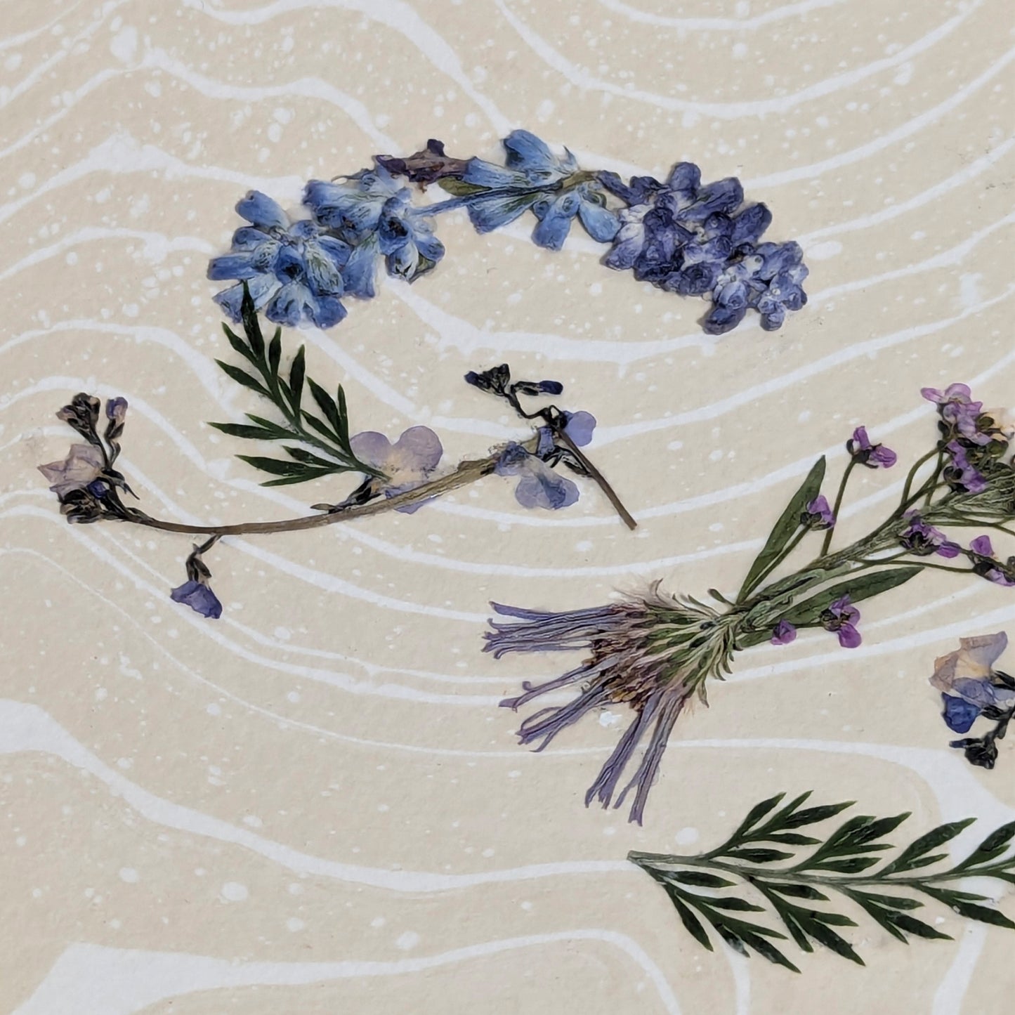 Close-up of pressed botanical elements forming letters "GIN" on Suminagashi marbled paper, detailed texture of floral word artwork