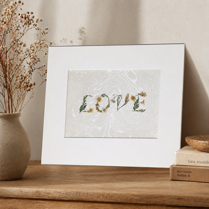 Framed “LOVE” botanical artwork made from pressed flowers on a Suminagashi marbled paper, styled on wooden surface with ceramic vase, dried florals, and stacked books.