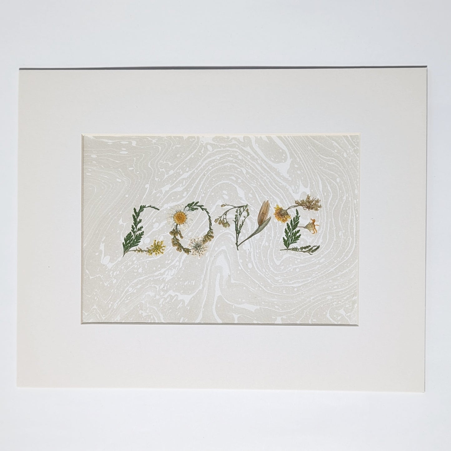 Pressed botanical “LOVE” artwork on taupe  Suminagashi marbled background, matted in white frame, handcrafted using real flowers in minimalist presentation.