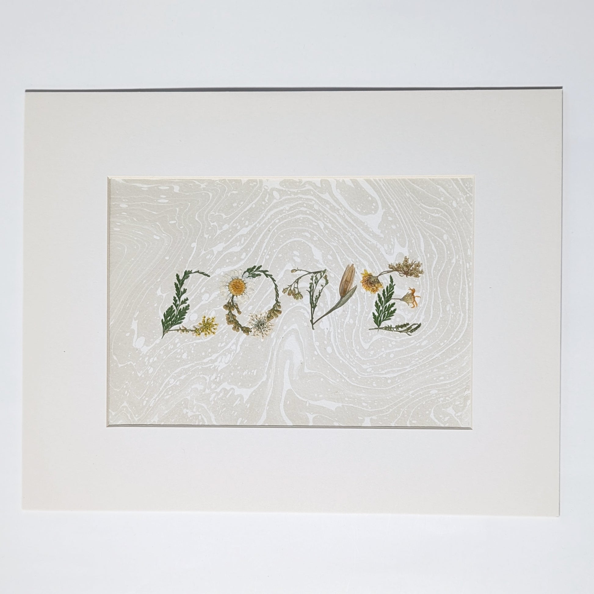 Pressed botanical “LOVE” artwork on taupe  Suminagashi marbled background, matted in white frame, handcrafted using real flowers in minimalist presentation.