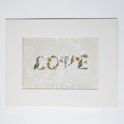Pressed botanical “LOVE” artwork on taupe  Suminagashi marbled background, matted in white frame, handcrafted using real flowers in minimalist presentation.