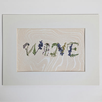 Pressed floral word “WINE” composed from real flowers on hand-marbled Suminagashi paper, framed botanical word art