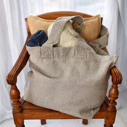 Natural linen tote bag styled on wooden chair filled with textiles in soft neutral setting
