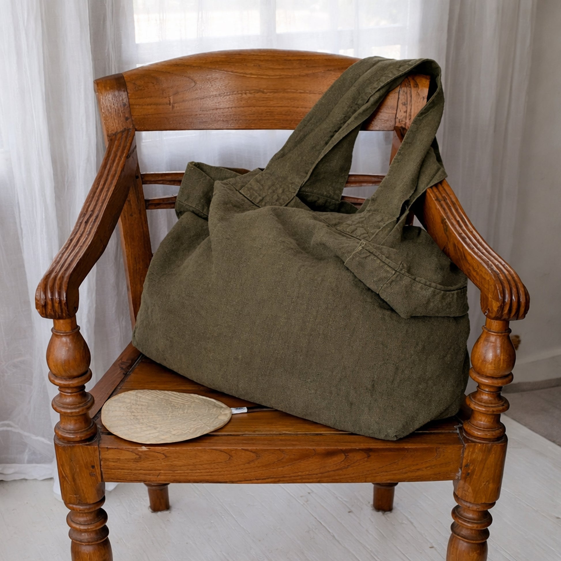 Olive linen tote bag draped over wooden chair with soft natural lighting