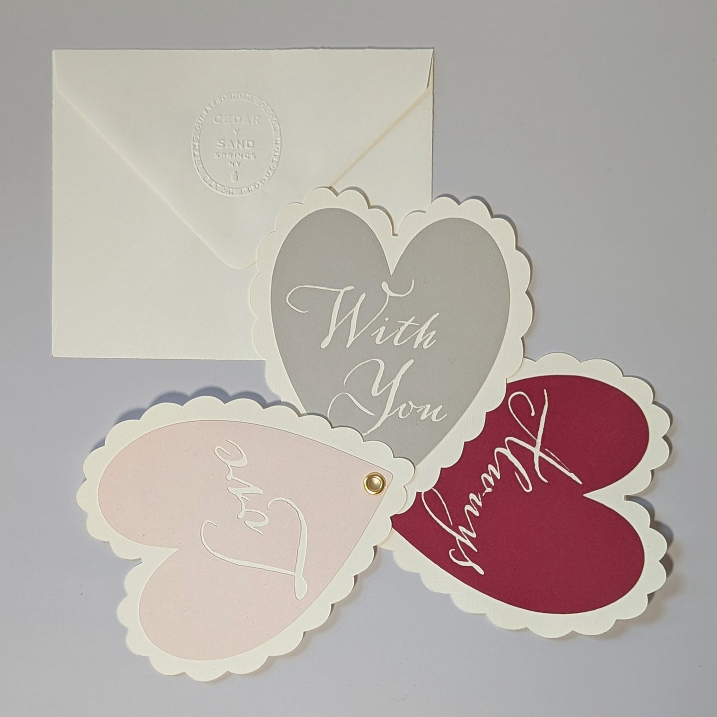 Heart-shaped notecard fanned outward showing LOVE, WITH YOU, ALWAYS cut-outs in blush, gray and merlot colors.