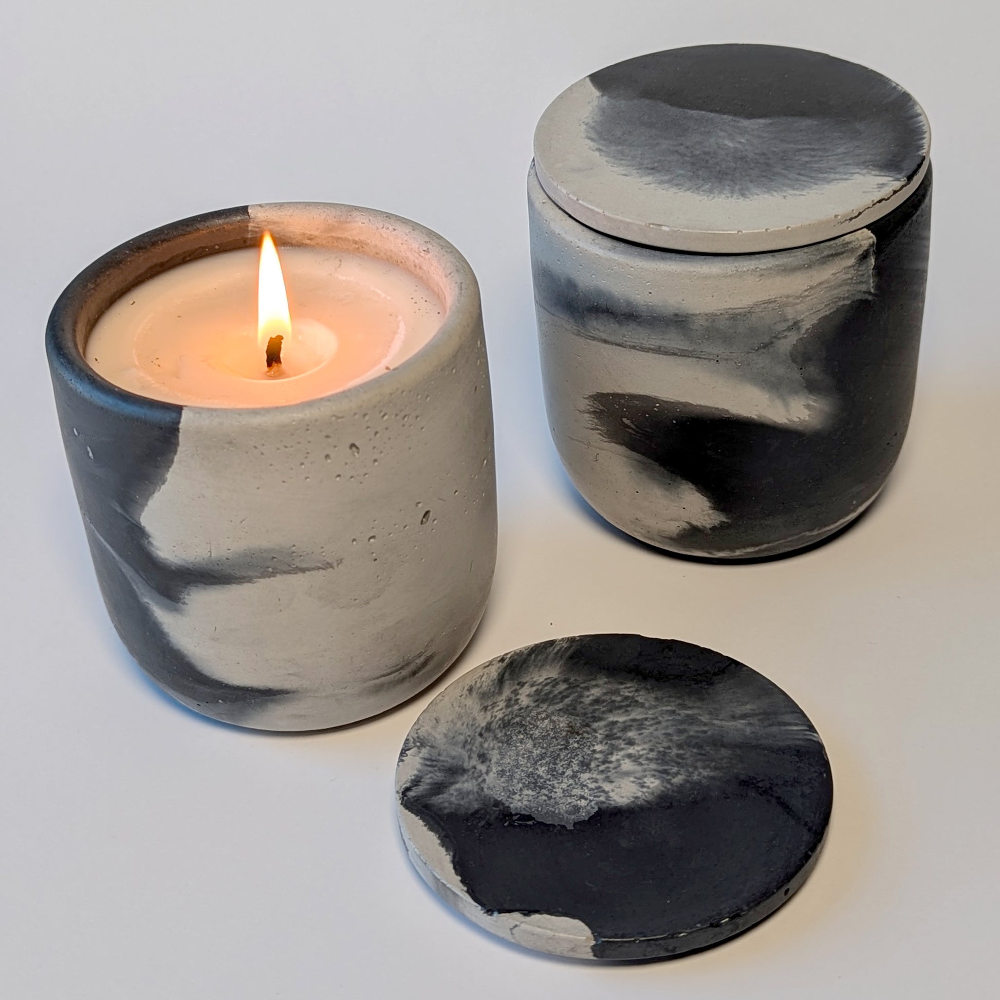 Nightcap Noir candle burning, flame glowing against the smoky cement vessel surface.