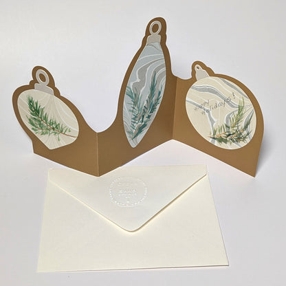 The back of the Suminagashi trifold ornament notecard, showing the marbled circular ornament panel and the CEDAR Y SAND embossed envelope beneath. Not for sale with personalization.