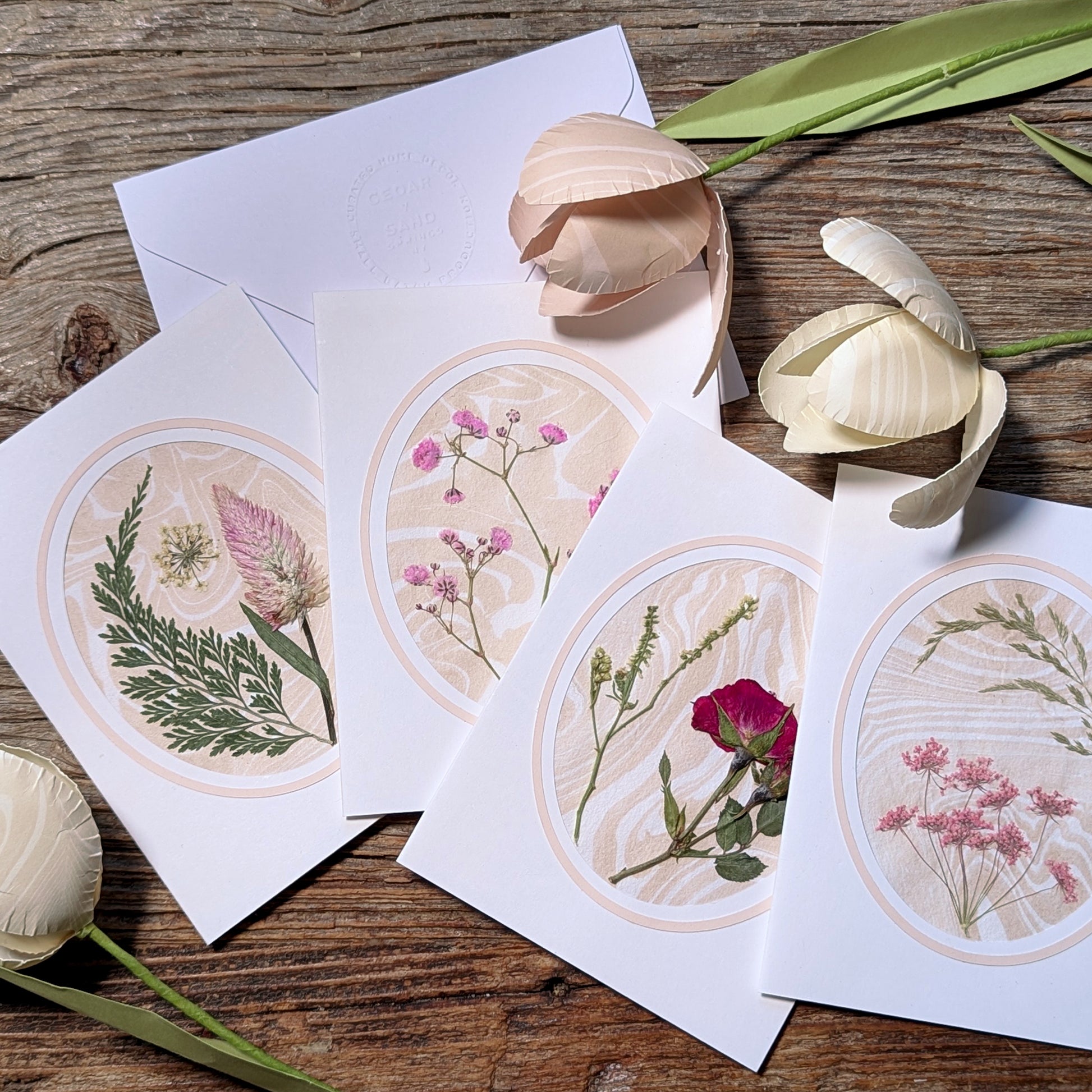 Suminagashi pressed flora notecards with wildflower designs arranged on rustic wood surface with tulips and embossed envelopes