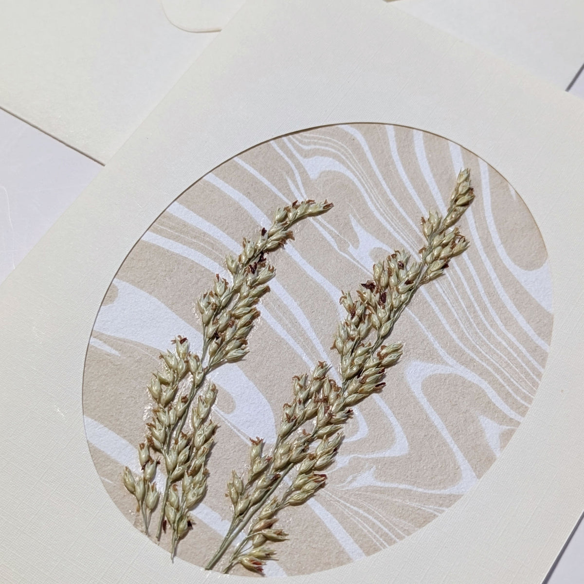 close-up of handmade Walking Dunes Dunegrass notecard with pressed dune grasses layered over neutral hand-marbled Suminagashi paper in an oval aperture.