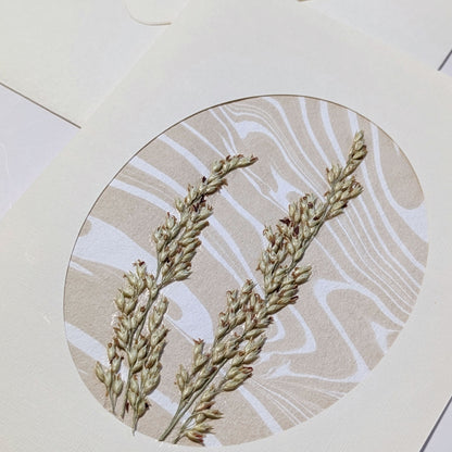 close-up of handmade Walking Dunes Dunegrass notecard with pressed dune grasses layered over neutral hand-marbled Suminagashi paper in an oval aperture.