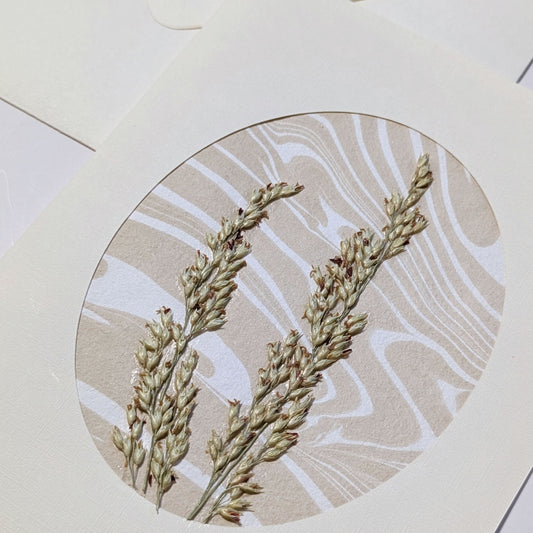 close-up of handmade Walking Dunes Dunegrass notecard with pressed dune grasses layered over neutral hand-marbled Suminagashi paper in an oval aperture.