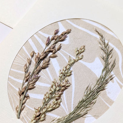 close-up of Walking Dunes Gathered pressed flora notecard with a composition of dried grasses in wheat, green and muted lavender over Suminagashi paper.