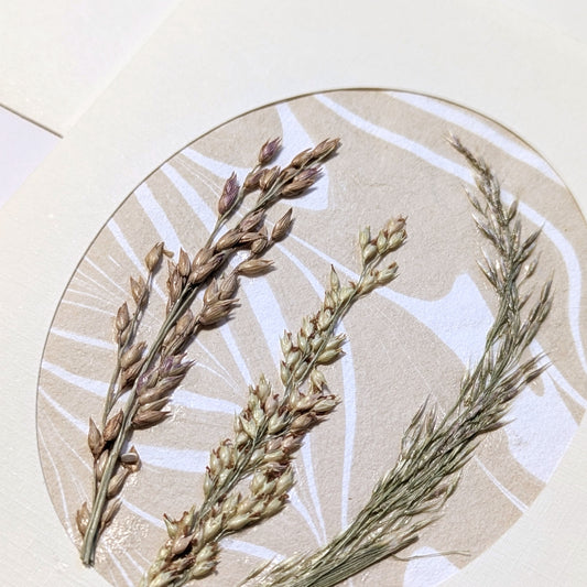 close-up of Walking Dunes Gathered pressed flora notecard with a composition of dried grasses in wheat, green and muted lavender over Suminagashi paper.