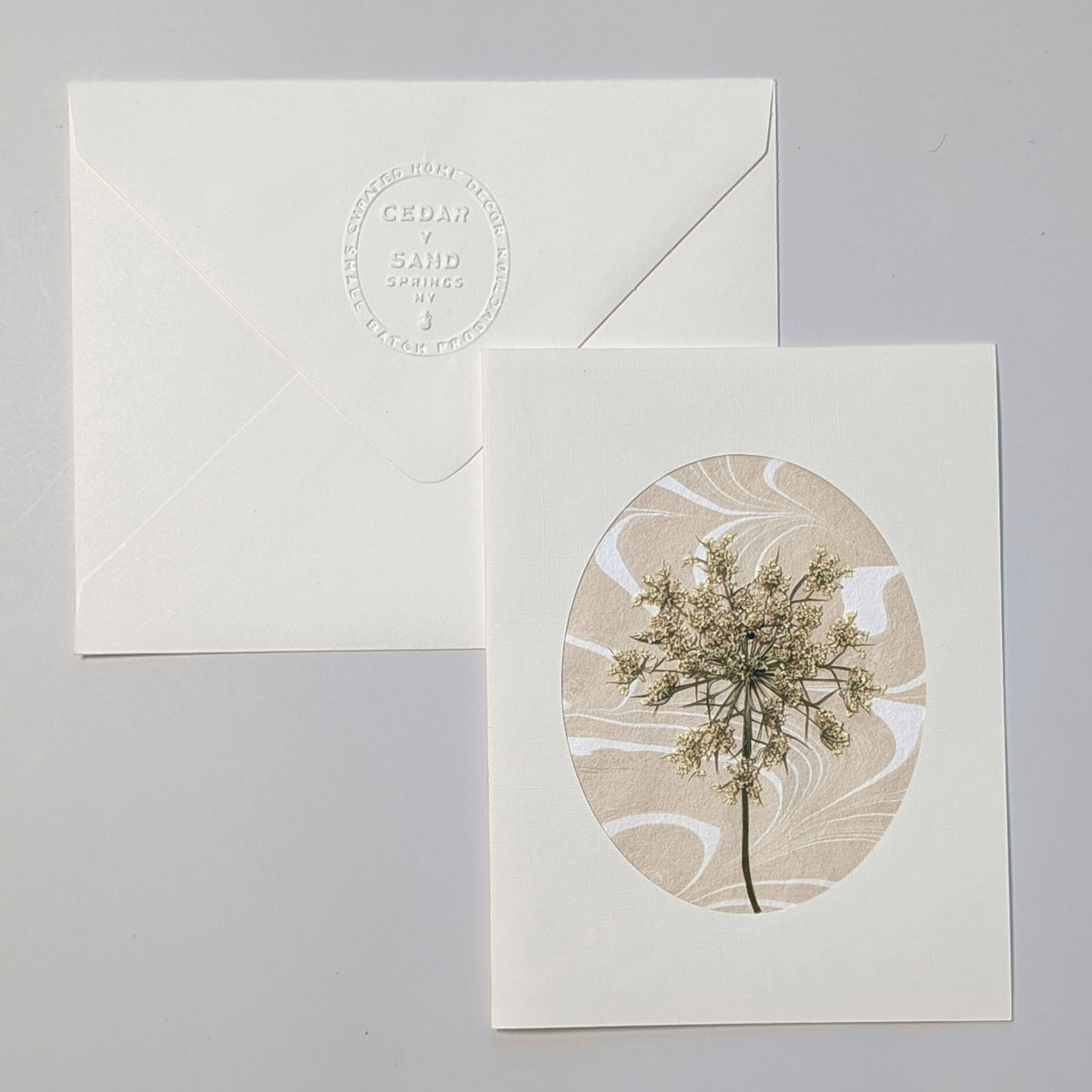 Walking Dunes Lace handmade notecard featuring a delicate pressed wildflower over warm neutral hand-marbled Suminagashi paper within an oval aperture.