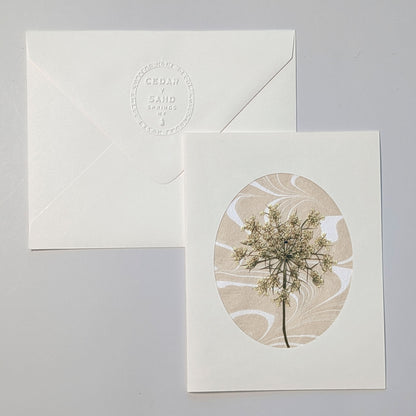 Walking Dunes Lace handmade notecard featuring a delicate pressed wildflower over warm neutral hand-marbled Suminagashi paper within an oval aperture.