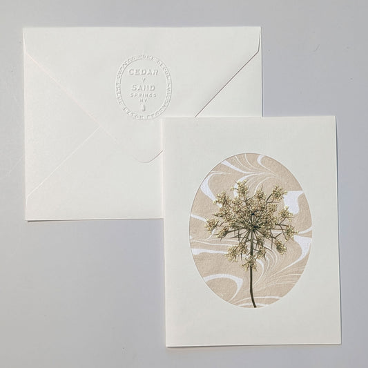 Walking Dunes Lace handmade notecard featuring a delicate pressed wildflower over warm neutral hand-marbled Suminagashi paper within an oval aperture.