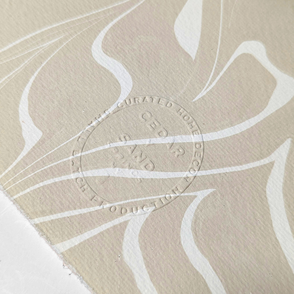 Close-up of embossed CEDAR Y SAND insignia on the reverse of hand-marbled Suminagashi paper, showing fine texture and flowing ink patterns.