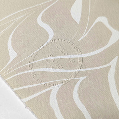 Close-up of embossed CEDAR Y SAND insignia on the reverse of hand-marbled Suminagashi paper, showing fine texture and flowing ink patterns.
