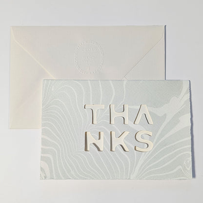 Suminagashi Springs Thanks Notecard in Mist, featuring pale blue-gray marbling, cut-out typography and natural Fabriano paper.