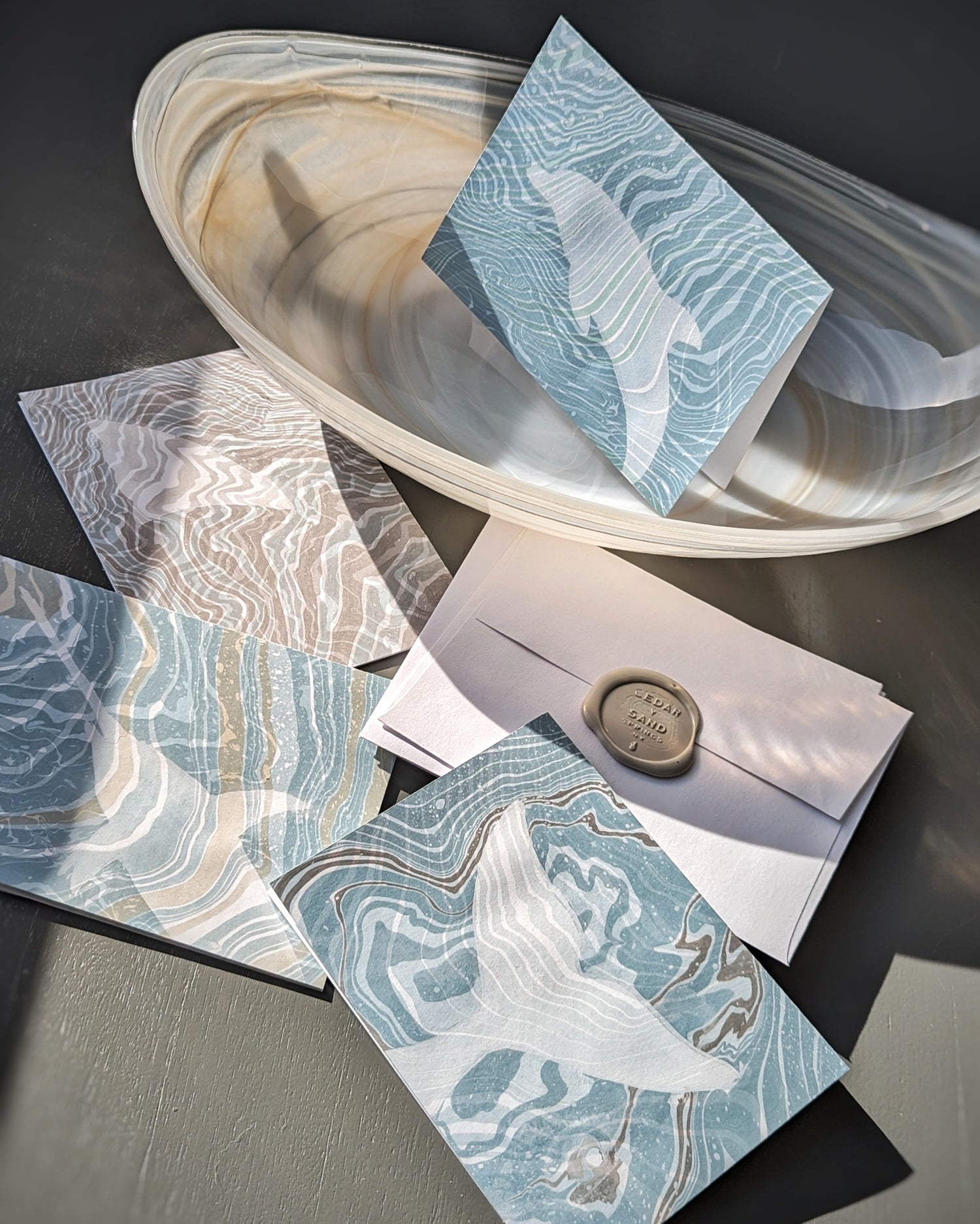Hand-marbled Suminagashi notecards with marine fauna displayed with matching envelopes sealed in wax, arranged in a seashell-inspired bowl.
