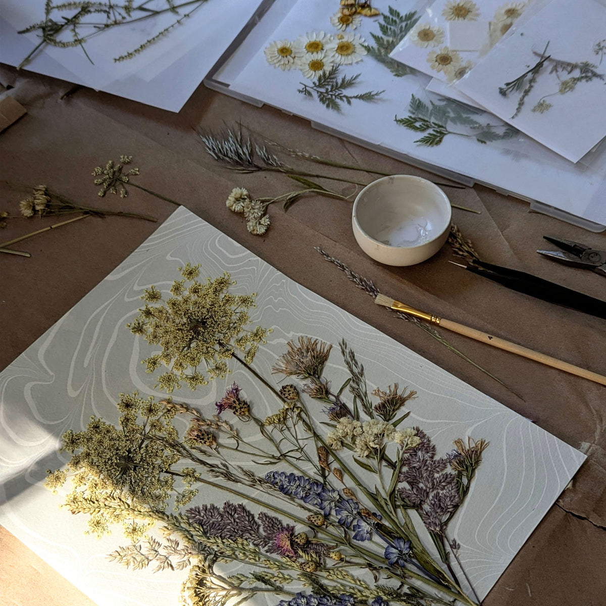 Dune Bouquet in progress in the CEDAR Y SAND East Hampton studio, with pressed botanicals being composed by hand over Suminagashi paper.