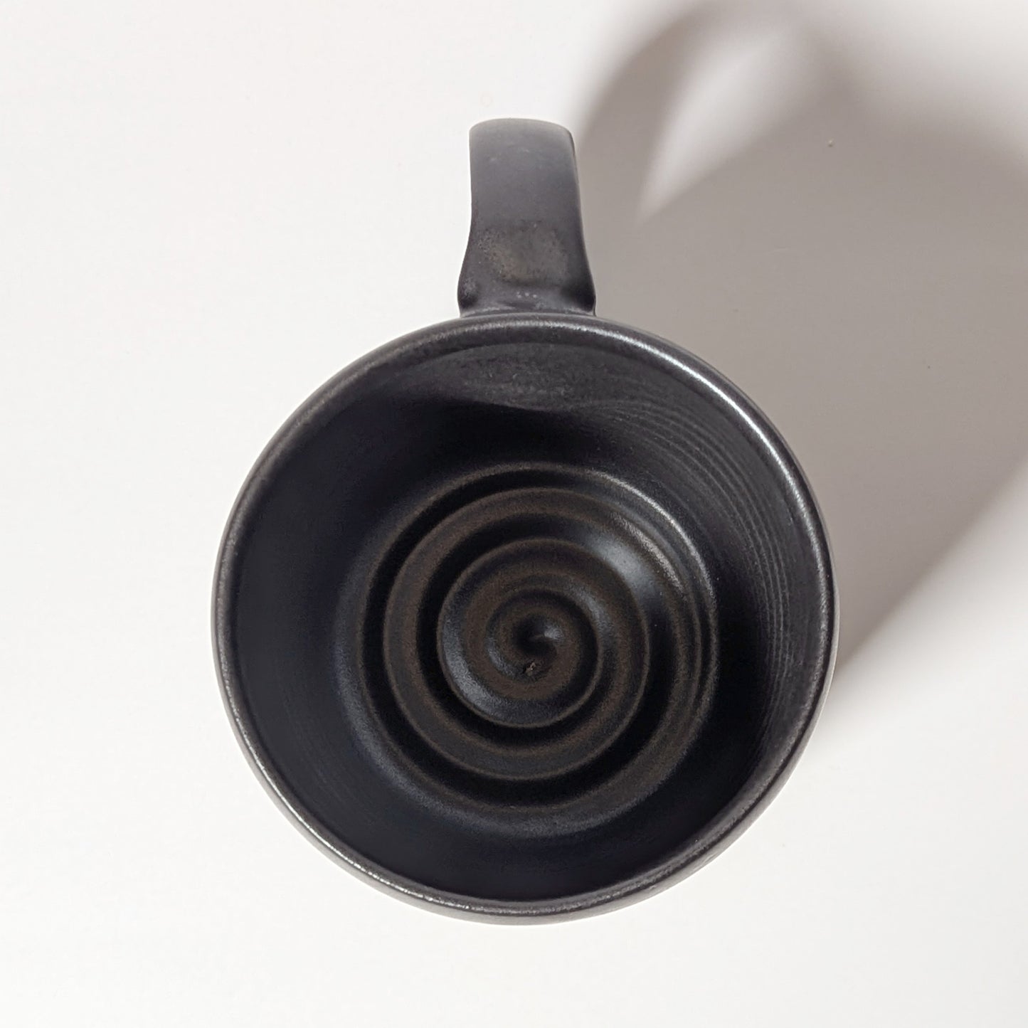 Top-down view of black ceramic mug revealing wheel-thrown spiral interior