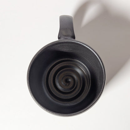 Top-down view of black ceramic mug revealing wheel-thrown spiral interior