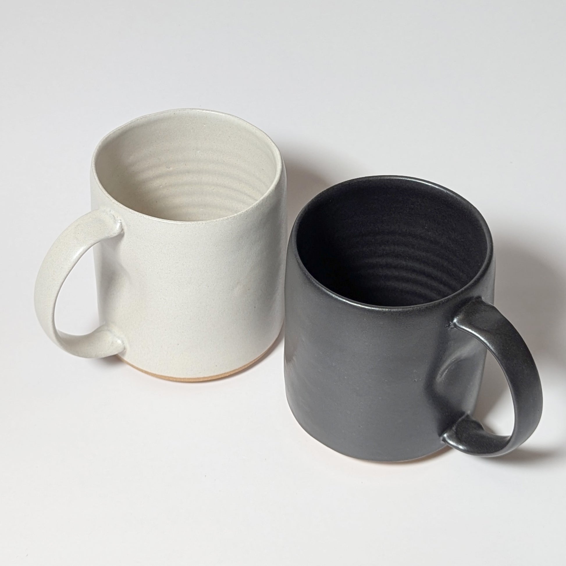 Black and off-white stoneware mugs displayed side by side against a white background, showing balanced minimalist forms