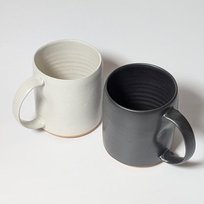 Black and off-white stoneware mugs displayed side by side against a white background, showing balanced minimalist forms